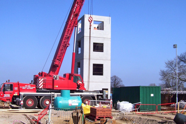 red mobile crane in front of progress installation of four-high precast concrete stair cores