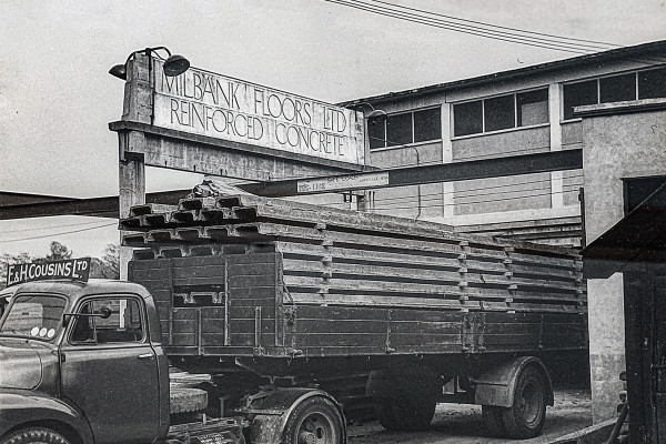 Historic image from 1947 of lorry carrying a load of concrete flooring in front of a sign which reads 'Milbank Floors Ltd, Reinforced Concrete'