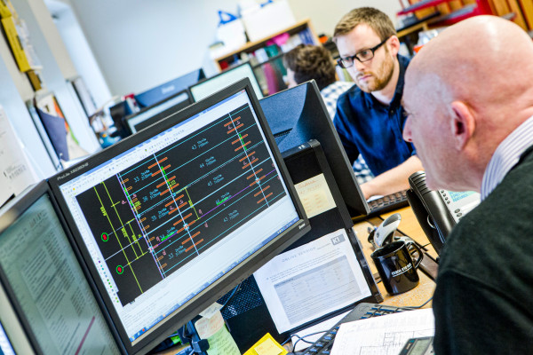 Workers in design office sit at computers with auto cad drawings open on screen