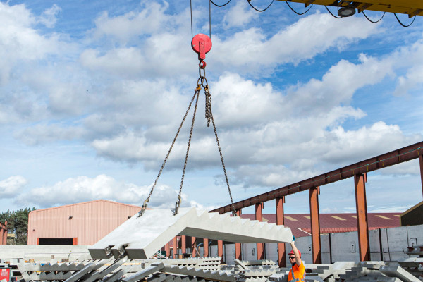 Crane lifting a precast concrete staircase and landing in factory yard surrounded by concrete staircases