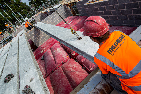 Milbank employee installing precast concrete flooring beams wearing bright organ vest and hard hat