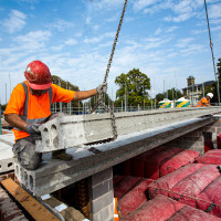 Milbank employee installing precast concrete flooring beams wearing bright organ vest and hard hat