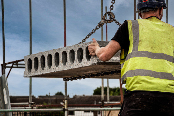 Person in yellow hi vis vest guiding hollowcore concrete slab in installation