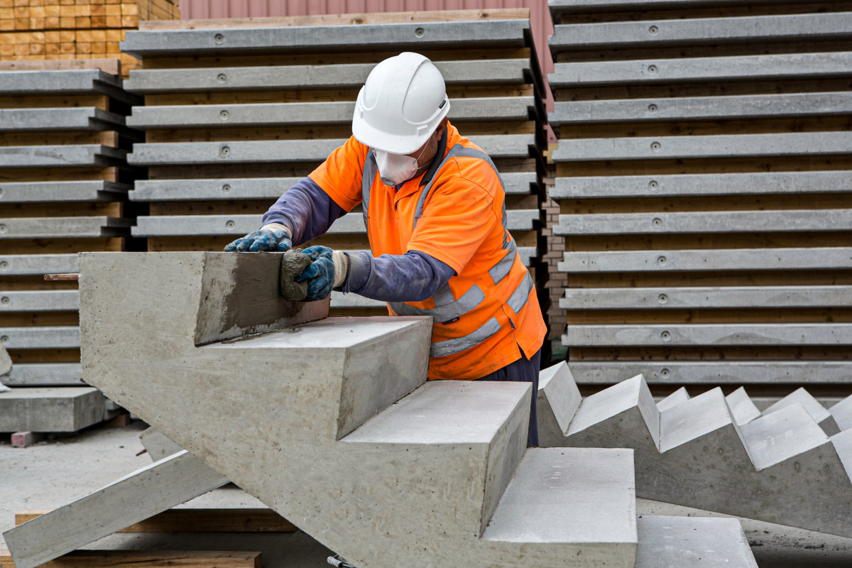 Milbank employee treating a precast concrete staircase while wearing a bright vest, mask and hard hat